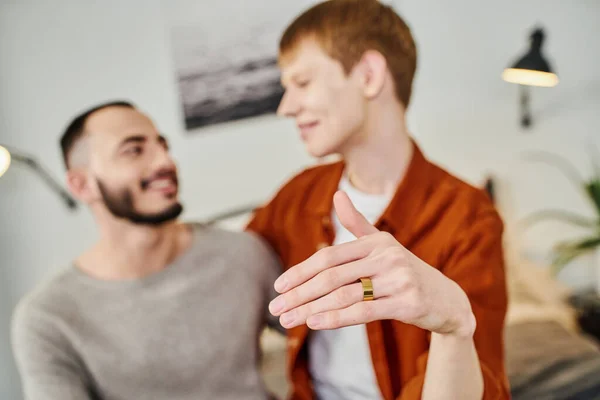 Borrosa gay hombre mostrando boda anillo cerca novio en casa - foto de stock