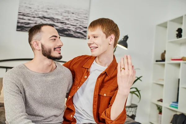Cheerful redhead gay man showing wedding ring near bearded boyfriend at home — Stock Photo