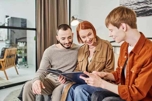 Redhead gay man showing photo album to boyfriend and amazed mother at home — Stock Photo