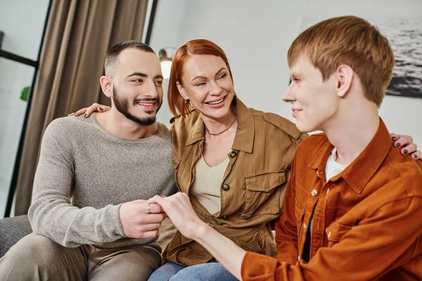 Overjoyed woman embracing young gay son and his partner at home — Stock Photo