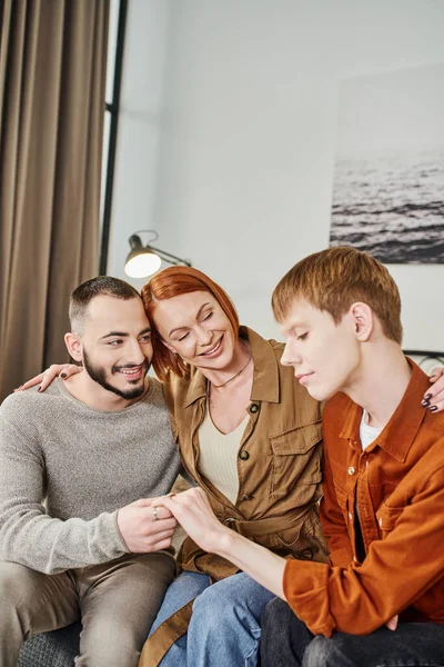 Smiling woman embracing young gay man and happy son showing wedding ring at home — Stock Photo