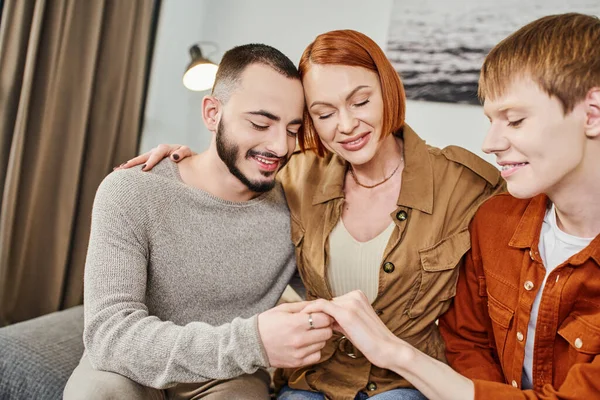 Joyful gay man showing wedding ring to happy mother and gay partner at home — Stock Photo
