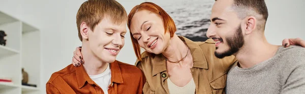 Gioiosa donna con gli occhi chiusi abbracciando sorridente gay uomo e figlio a casa, striscione — Foto stock