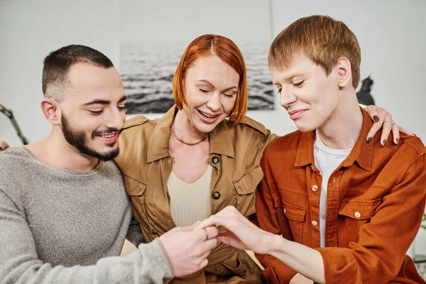 Young gay man showing wedding ring near boyfriend and excited mother at home — Stock Photo