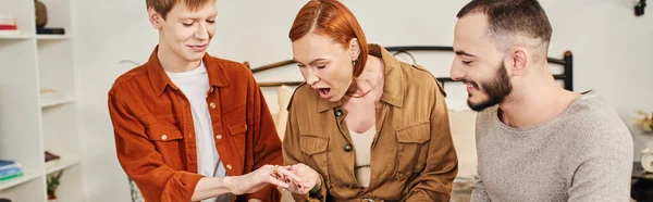 Happy gay man showing wedding ring to astonished mother near bearded boyfriend at home, banner — Stock Photo