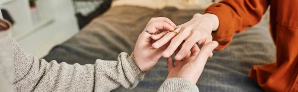 Cropped view of gay man wearing wedding ring on hand of boyfriend while making marriage proposal at home, banner — Stock Photo
