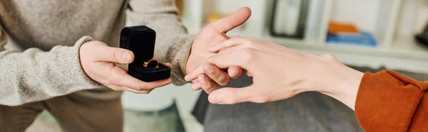 Partial view of young man holding jewelry box with wedding ring and making marriage proposal to gay partner at home, banner — Stock Photo
