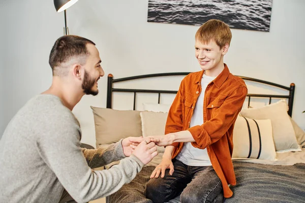 Young bearded gay man making marriage proposal to happy boyfriend sitting on bed at home — Stock Photo