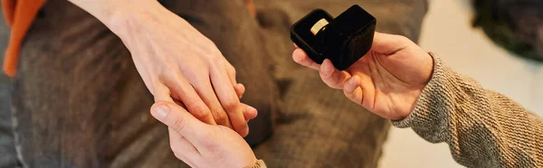 Vue partielle de l'homme gay tenant boîte à bijoux avec anneau de mariage et tenant la main du petit ami tout en faisant la demande en mariage, bannière — Photo de stock