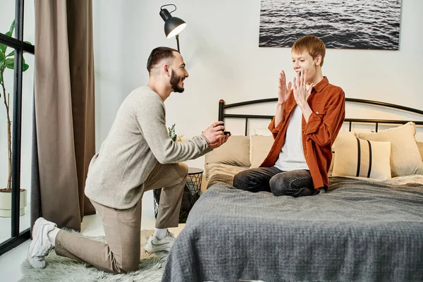 Здивований гей-чоловік показує вау жест біля хлопця, роблячи шлюбну пропозицію в спальні — стокове фото