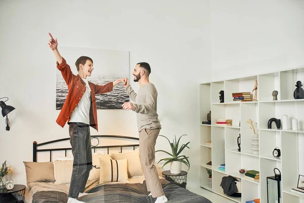 Overjoyed gay couple having fun while standing on bed at home — Stock Photo