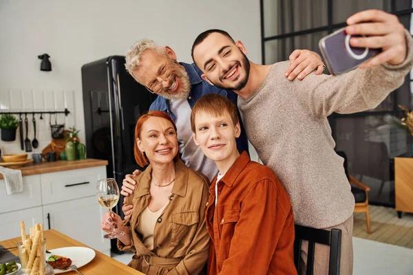 Alegre homem tomando selfie com gay parceiro e pais durante família ceia no cozinha — Fotografia de Stock