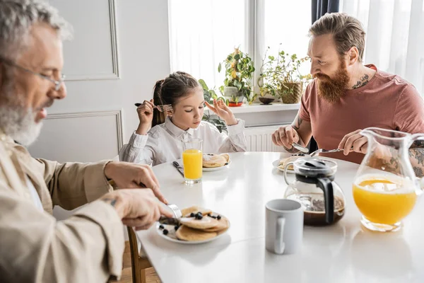 Preadolescente chica desayunando con gay padres en casa en la mañana - foto de stock