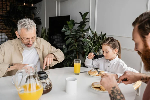Pareja gay desayunando con hija adoptiva en casa - foto de stock