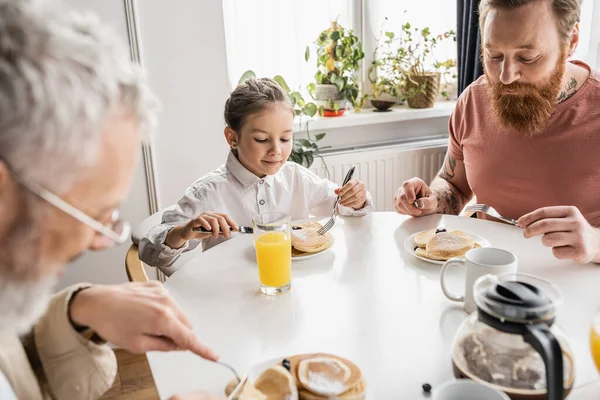 Preteen girl looking at pancakes near homosexual parents at home — Stock Photo