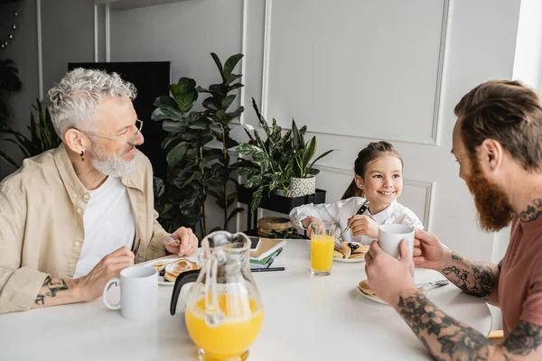 Cheerful preteen girl looking at homosexual dad near breakfast at home — Stock Photo