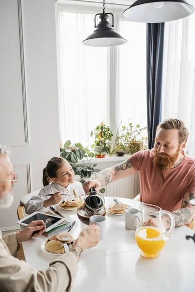 Gay man pouring coffee near partner and daughter during breakfast at home — Stock Photo