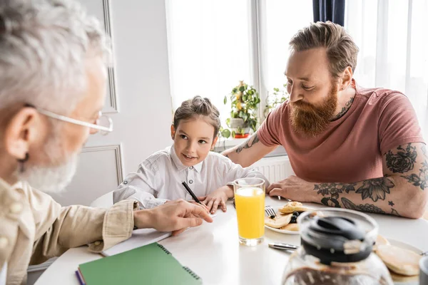 Preteen girl writing on notebook near homosexual parents and pfannkuchen at home — Stockfoto
