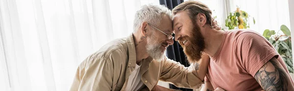 Усміхнений гей чоловік обіймає татуйованого партнера вдома, банер — стокове фото