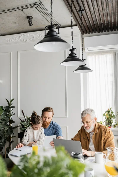 Gay father doing homework with daughter near partner using laptop at home — Stock Photo