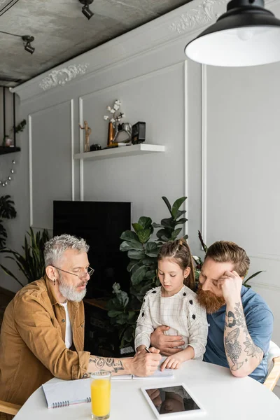 Gay man writing on notebook near partner and preteen daughter at home — Stock Photo