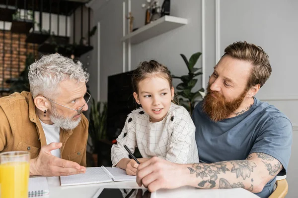 Gay fathers talking to smiling preteen daughter doing homework at home — Stock Photo