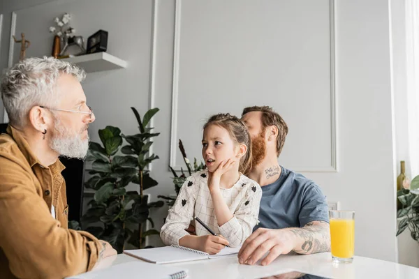Preteen girl talking to gay parents while doing homework at home — Stock Photo