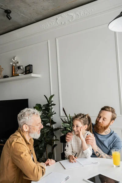 Smiling girl doing homework with same sex dads near digital tablet with blank screen at home — Stock Photo