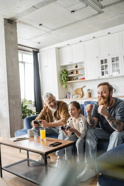 KIEW, UKRAINE - 19. April 2023: Schwuler Mann spielt Videospiel mit Tochter in der Nähe eines fröhlichen Partners zu Hause — Stockfoto