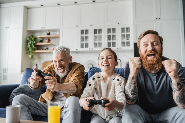 KYIV, UKRAINE - APRIL 19, 2023: Excited gay man sitting near daughter and partner playing video game at home — Stock Photo