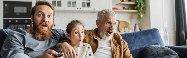 Шокированные родители-геи и дочка-подросток смотрят телевизор дома, баннер — стоковое фото
