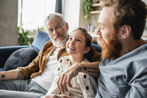 Carefree preteen girl talking to gay parents in living room — Stock Photo