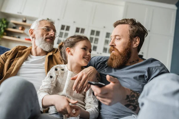 Smiling child talking to same sex fathers with remote controller at home — Stock Photo