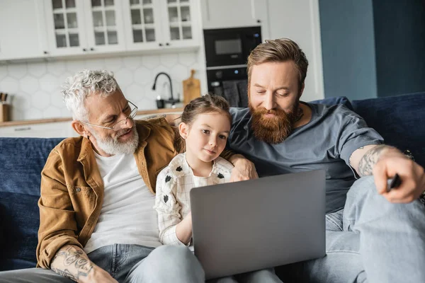 Preteen child using laptop near tattooed gay fathers at home — Stock Photo