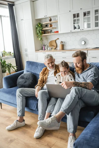 Homosexual fathers using laptop with cheerful preteen daughter at home — Stock Photo