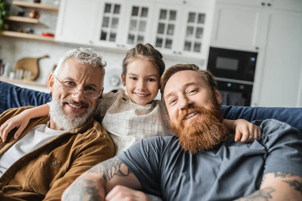 Portrait of smiling preteen kid hugging same sex parents at home — Stock Photo