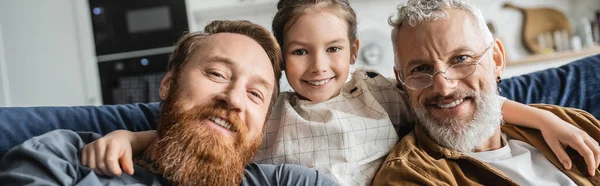 Carefree preteen girl hugging bearded gay fathers on couch at home, banner — Stock Photo