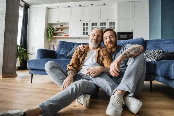 Sorrindo gay homens olhando para câmera enquanto sentado no chão em casa — Fotografia de Stock