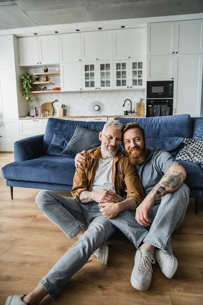 Positive homosexual man hugging tattooed partner on floor at home — Stock Photo