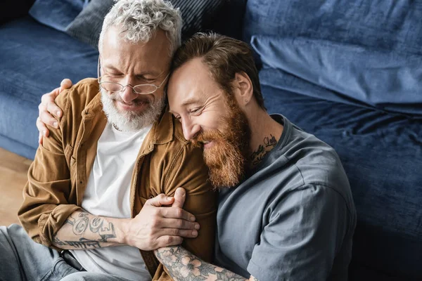 High angle view of tattooed gay man holding hand of smiling partner in living room — Stock Photo