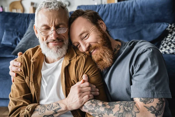 Porträt eines lächelnden homosexuellen Mannes, der einen reifen Partner zu Hause umarmt — Stockfoto