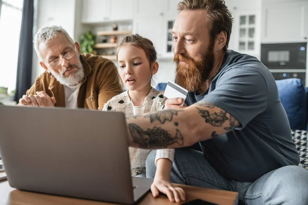 Homosexuelle Eltern mit Kreditkarte mit Laptop in der Nähe ihrer Tochter im Wohnzimmer — Stockfoto