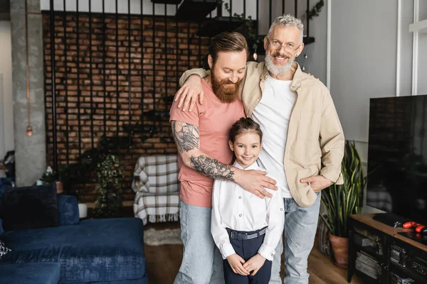 Smiling homosexual couple hugging preteen daughter at home — Stock Photo