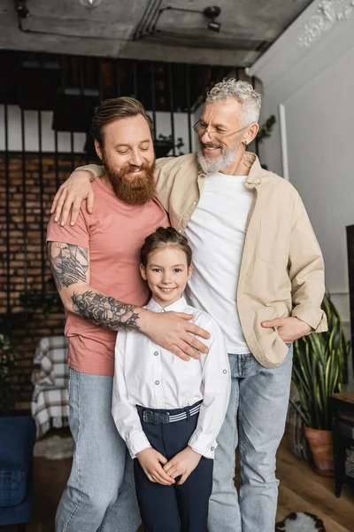 Cheerful homosexual couple hugging adopted preteen child at home — Stock Photo