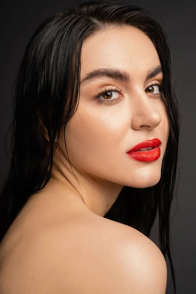 Portrait of young and pretty woman with wet brunette hair and red lips posing with bare shoulders while looking at camera after shower isolated on grey background — Stock Photo