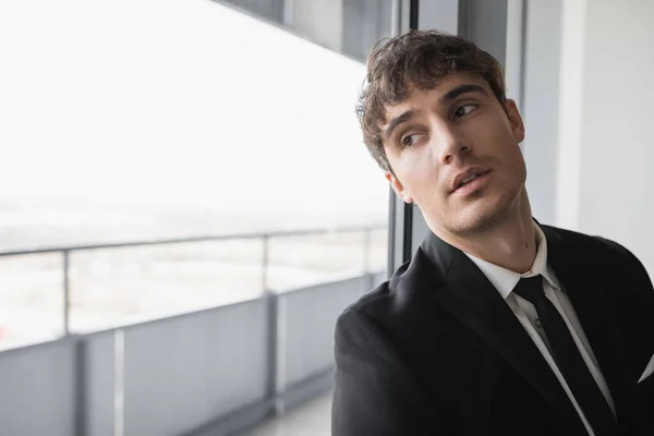 Dreamy man in classic formal wear with black tie and white shirt standing in modern hotel room and looking at window, groom on wedding day, special occasion — Stock Photo