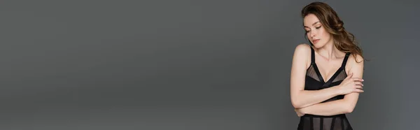 Modisches junges brünettes Model mit Frisur und natürlichem Make-up posiert in sexy schwarzen und formschlüssigen Body und schaut isoliert auf grau mit Kopierraum, Banner — Stockfoto