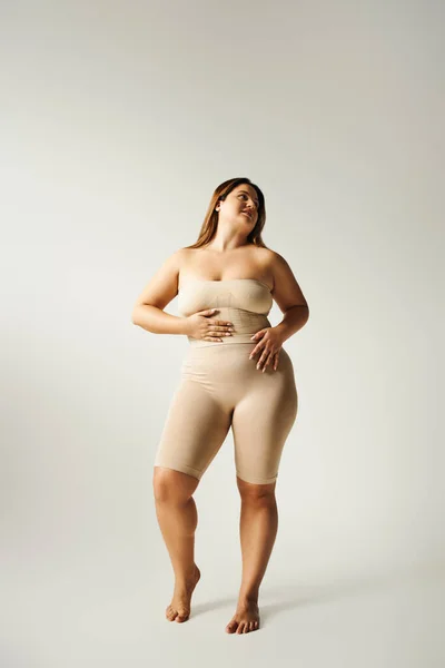 Full length of barefoot and happy woman with plus size body posing in strapless top with bare shoulders and underwear on grey background in studio, body positive, self-love, figure type — Stock Photo