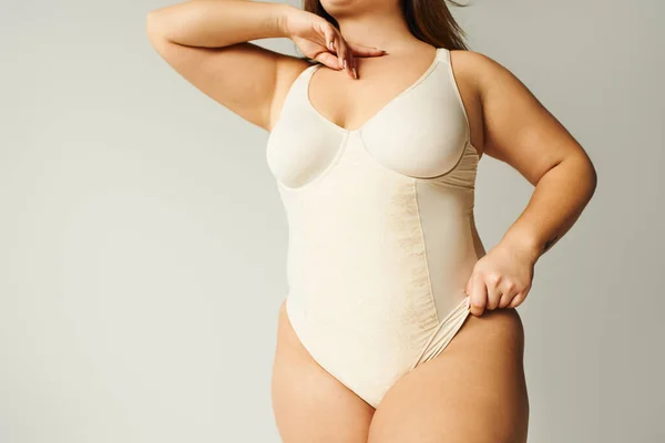 Partial view of brunette plus size woman in beige bodysuit posing while standing in studio on grey background, body positive, figure type, self-esteem, tattoo translation: harmony — Stock Photo