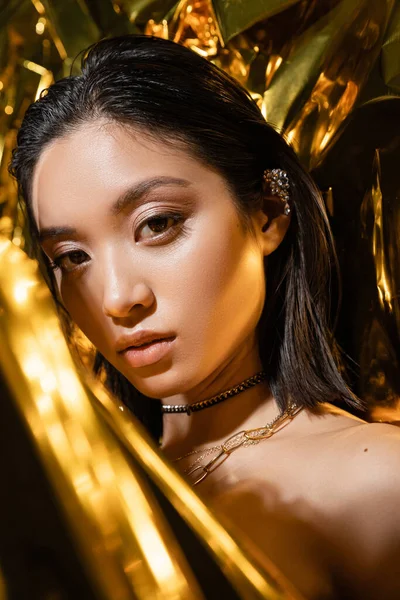 Porträt der verführerischen asiatischen jungen Frau mit nassen kurzen Haaren posiert neben glänzend gelbem Hintergrund, Modell, Blick in die Kamera, faltige Goldfolie, natürliche asiatische Schönheit — Stockfoto